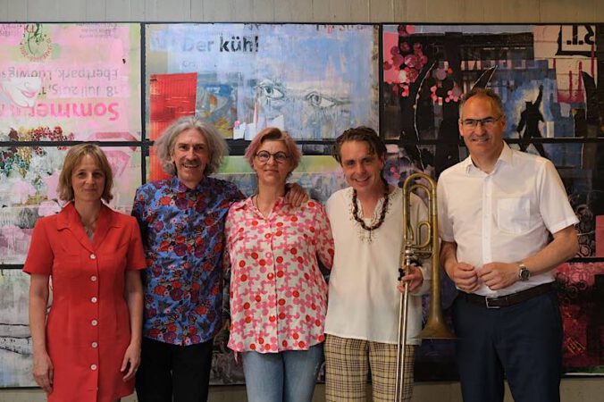 Die Künstlerin Anja Roth (Mitte) bei der Ausstellungseröffnung mit Landrat Dietmar Seefeldt, Musiker Bernhard Vanecek, Partner Herbert Pauser und Simone Maria Dietz (von rechts). Die Gruppe steht vor dem Triptychon, das Teil der Ausstellung ist. (Foto: KV SÜW)