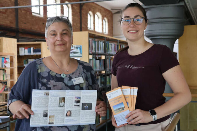 Beigeordnete Lena Dürphold (rechts) und Sabine Schäfe r, eine der beiden Bib liotheksleiterinnen, mit dem Programmflyer für das zweite H albjahr . (Quelle: Stadt Landau)