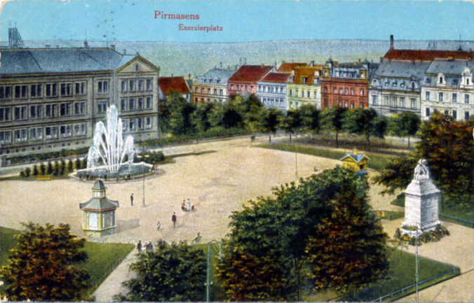 Impressionen aus den 1920er-Jahren: Blick auf den Exerzierplatz mit dem 1879 erbauten Schulhaus samt Springbrunnen, dem Bismarckdenkmal sowie den beiden Pavillons, wo es das legendäre Klickerwasser zu kaufen gab. (Foto: Sammlung Lehnung / Stadtarchiv Pirmasens)