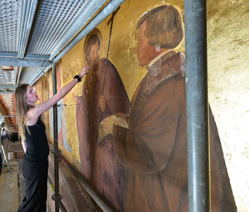 Anne Lackner, Diplomandin am Lehrstuhl für Kunsttechnologie, Konservierung und Restaurierung von Wandmalerei an der Hochschule für Bildende Künste in Dresden, erläutert die Schadensphänomene am Wandgemälde von Johann Baptist Schraudolph in der Vorhalle des Speyerer Domes. (Quelle: Domkapitel Speyer, Foto: Klaus Landry)